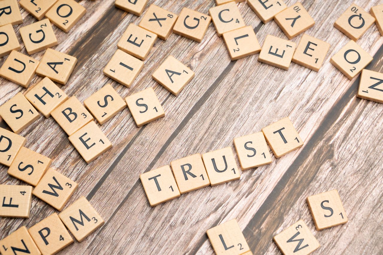 Services Scrabble letter tiles form the word 'Trust' on a wooden table, surrounded by scattered tiles.