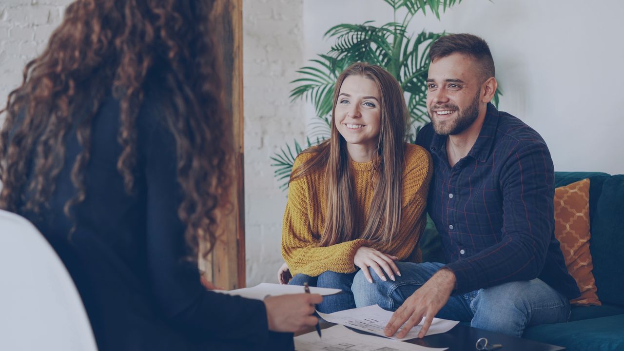 Services Couple discussing home options with agent in modern office setting.