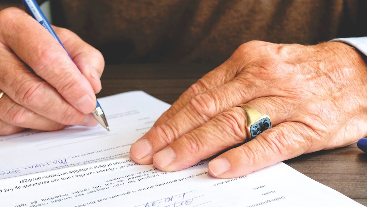 Services Close-up of a senior adult signing a legal document with a focus on hand and gold ring.